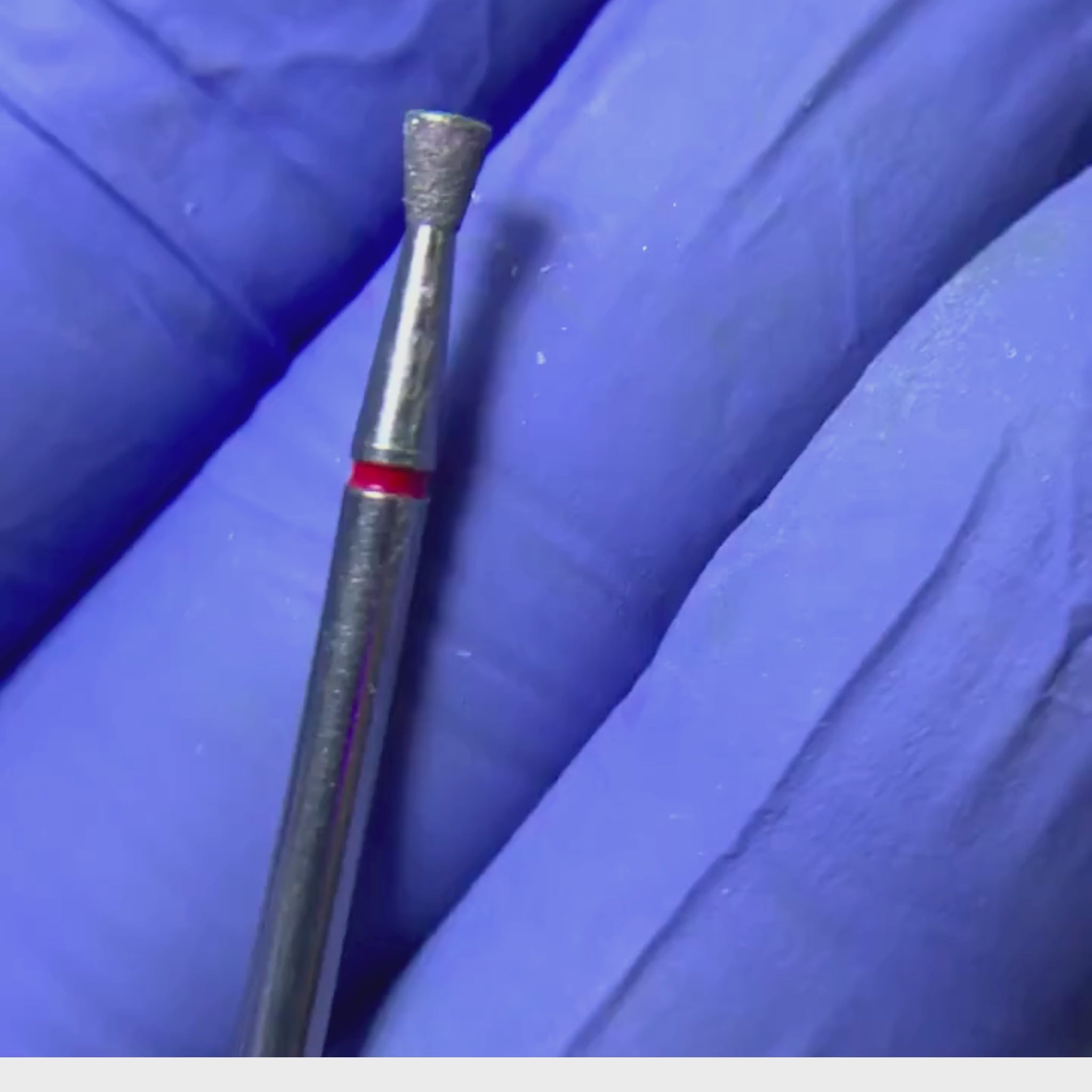 Primer plano de una broca de manicura con forma de cono inventido banda roja.